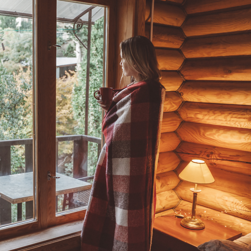 Femme dans un chalet cocooning enroulée dans une plaid avec une tasse à la main